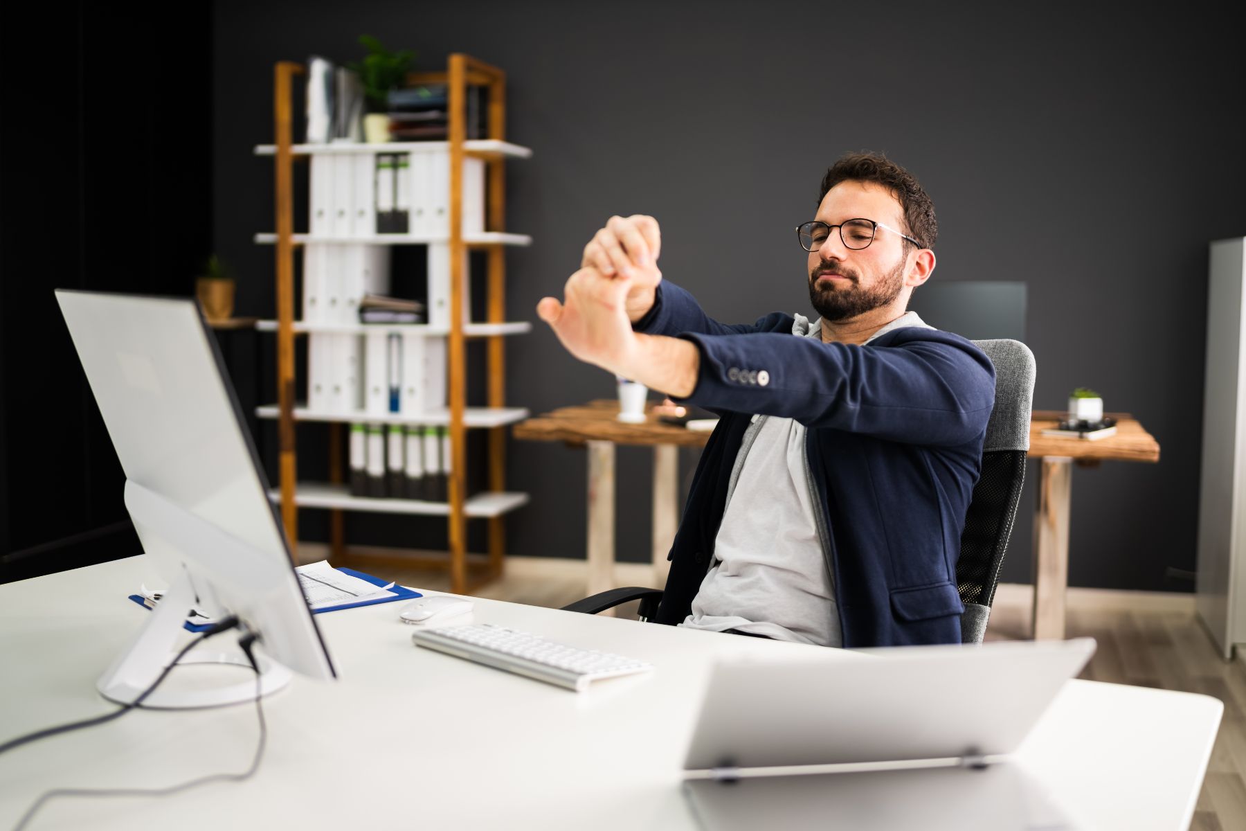 Man stretching his arms at a desk in an office, counteracting the effects of sitting all day at work